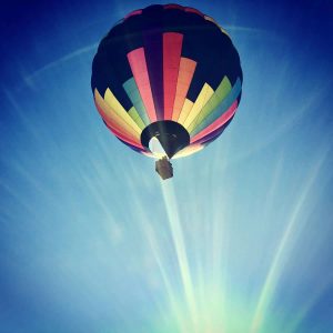 Hot air balloon flying overhead with beautiful sun rays