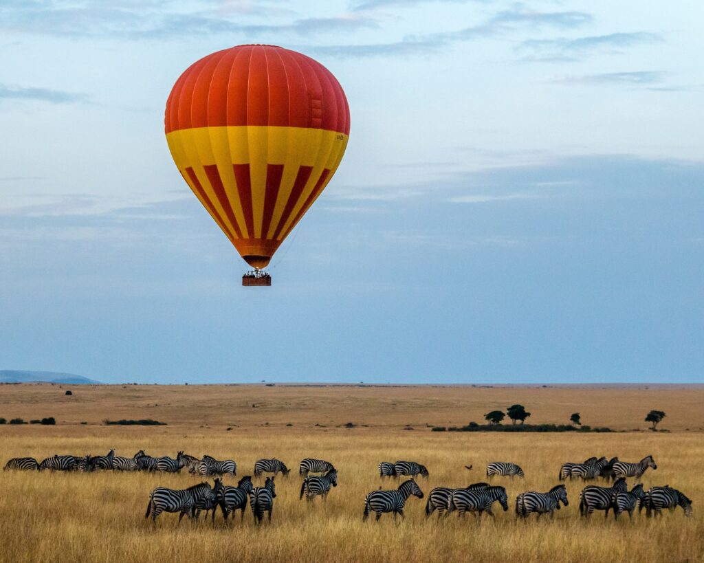 Red hot air balloon drifting over the Serengeti over a field of zebras.